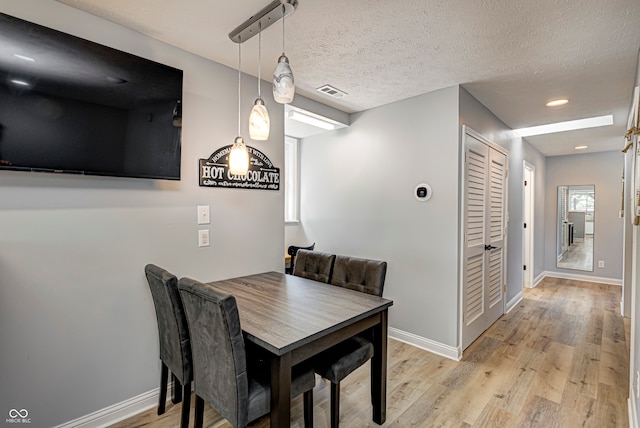 dining space featuring light wood-type flooring and a textured ceiling