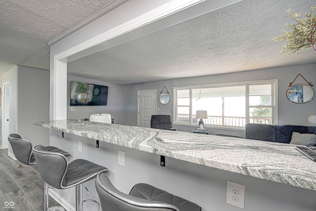 kitchen featuring a kitchen bar, a wealth of natural light, hardwood / wood-style floors, and a textured ceiling