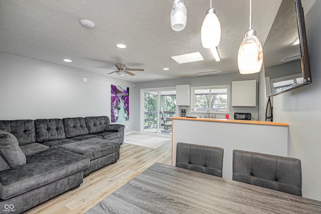 living room featuring a textured ceiling, light hardwood / wood-style flooring, ceiling fan, and a skylight