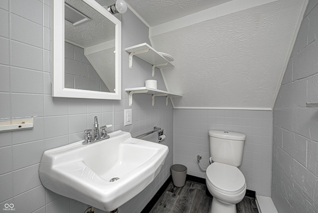 7587 Shady Side Dr, Bloomington, IN 47401 - bathroom featuring toilet, a sink, wood finished floors, a textured ceiling, and tile walls