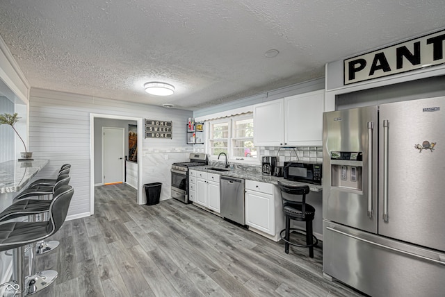 kitchen with white cabinets, light wood-type flooring, appliances with stainless steel finishes, sink, and a textured ceiling