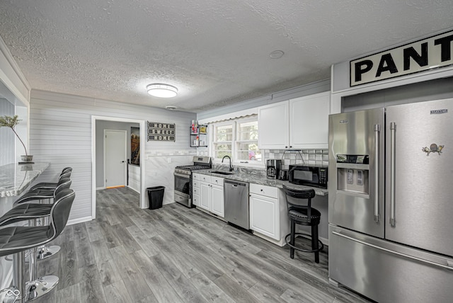 7587 Shady Side Dr, Bloomington, IN 47401 - kitchen with white cabinetry, light wood-type flooring, stainless steel appliances, a sink, and stone counters
