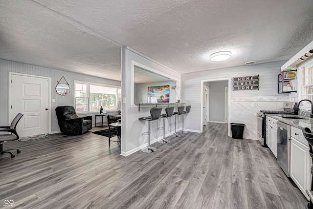 kitchen with white cabinets, appliances with stainless steel finishes, light stone countertops, wood-type flooring, and a textured ceiling