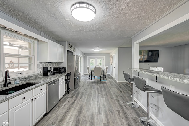 kitchen with light hardwood / wood-style flooring, appliances with stainless steel finishes, sink, a healthy amount of sunlight, and white cabinets