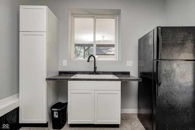 kitchen featuring black refrigerator, sink, and white cabinets