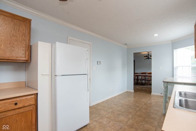 kitchen with ornamental molding, white refrigerator, an inviting chandelier, and sink