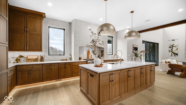 kitchen featuring decorative light fixtures, a kitchen island with sink, light hardwood / wood-style floors, and sink