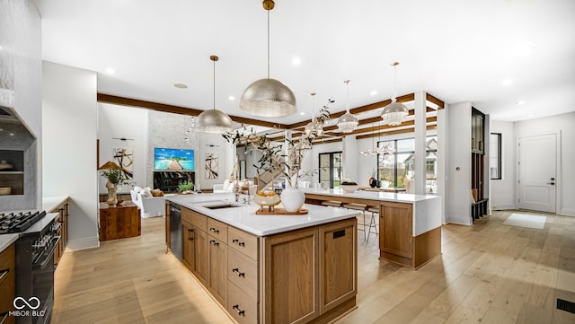 kitchen featuring a spacious island, range with gas stovetop, open floor plan, light countertops, and light wood-type flooring