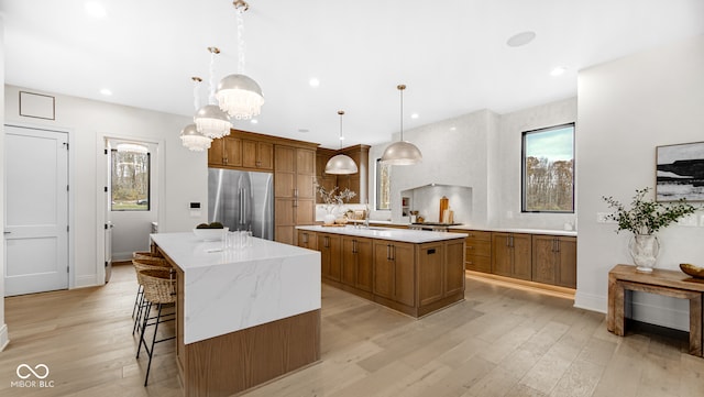 kitchen with light wood-style floors, a spacious island, stainless steel fridge, and brown cabinets