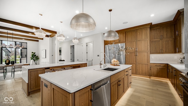 kitchen featuring appliances with stainless steel finishes, brown cabinetry, a kitchen island with sink, and a sink