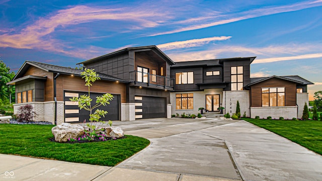 contemporary home featuring a balcony, driveway, a garage, and brick siding