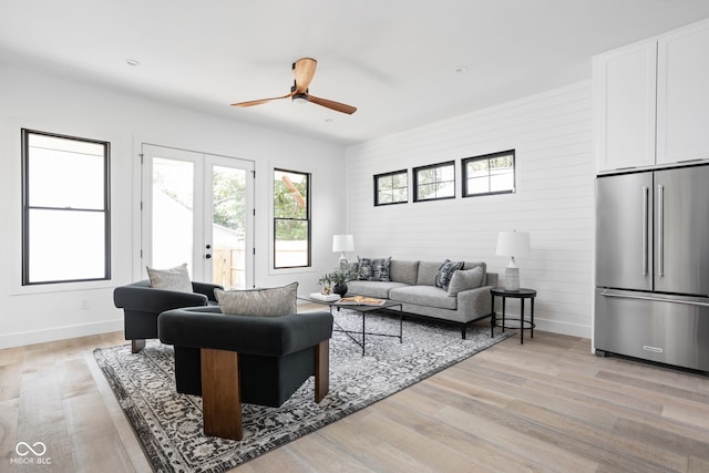 living room with ceiling fan, wooden walls, light hardwood / wood-style floors, and french doors