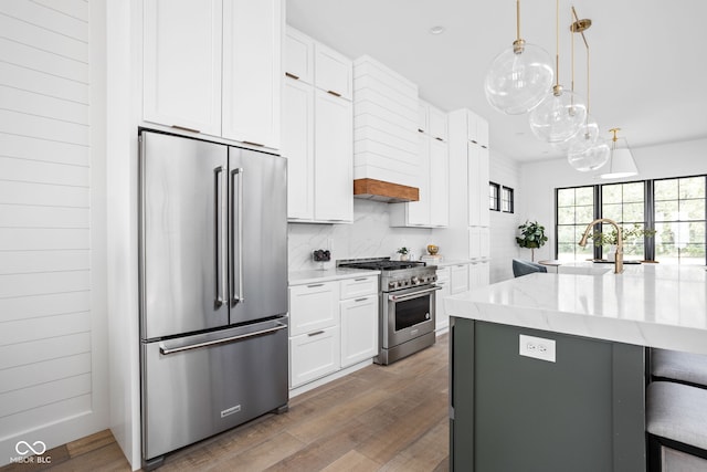 kitchen with high quality appliances, light hardwood / wood-style flooring, light stone countertops, hanging light fixtures, and white cabinets