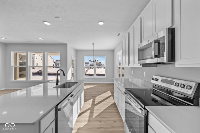 kitchen with appliances with stainless steel finishes, light wood-type flooring, white cabinets, decorative light fixtures, and sink