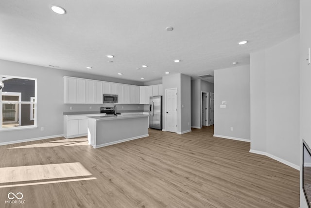 kitchen with appliances with stainless steel finishes, light wood-type flooring, an island with sink, sink, and white cabinetry