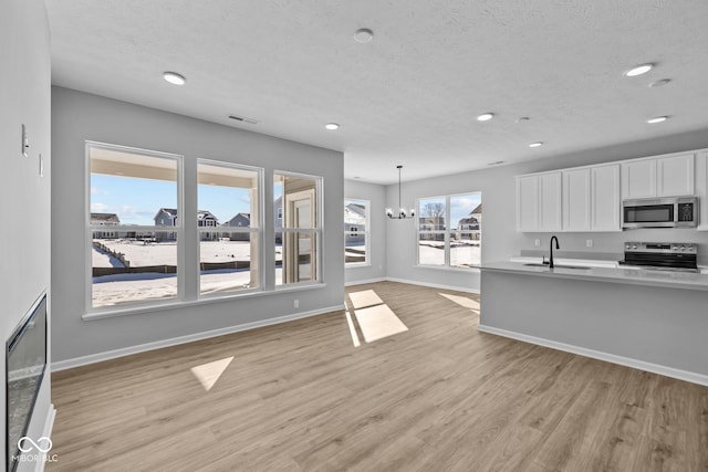 kitchen with light hardwood / wood-style floors, sink, appliances with stainless steel finishes, white cabinets, and pendant lighting