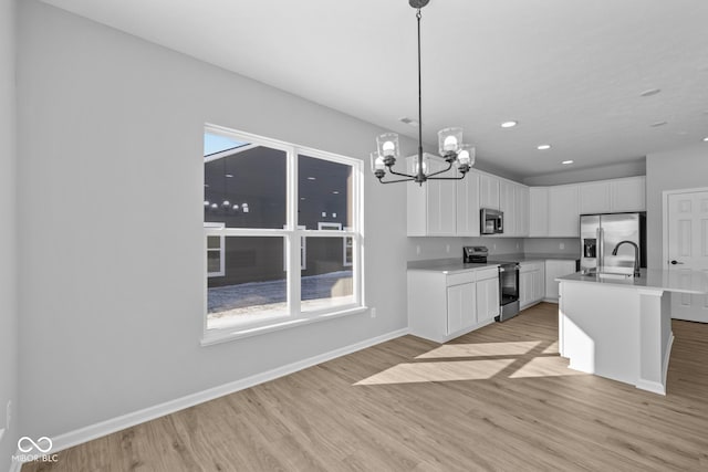 kitchen featuring white cabinetry, an island with sink, light wood-type flooring, hanging light fixtures, and appliances with stainless steel finishes