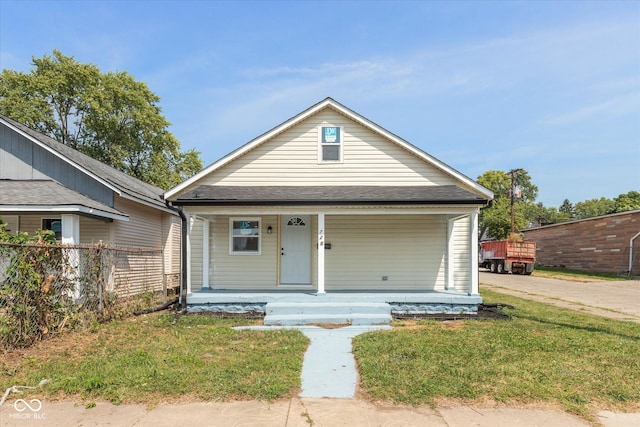 view of front facade featuring a shingled roof, a front yard, covered porch, and fence