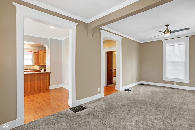 empty room featuring crown molding, sink, ceiling fan, and light colored carpet