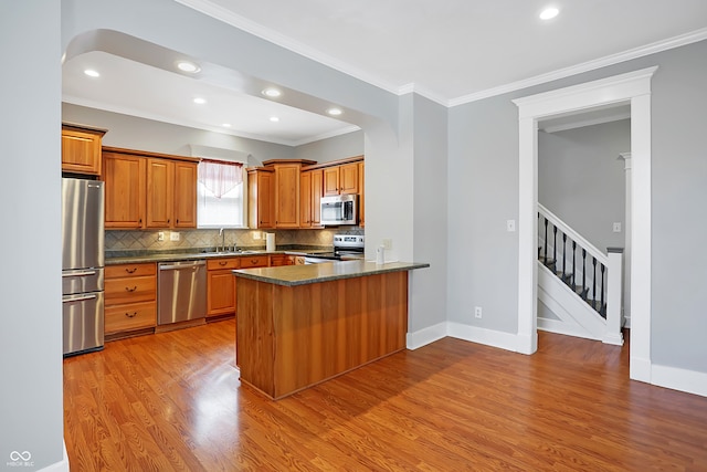 kitchen featuring appliances with stainless steel finishes, kitchen peninsula, ornamental molding, sink, and hardwood / wood-style flooring