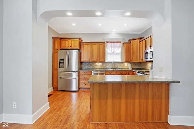 kitchen featuring crown molding, appliances with stainless steel finishes, light hardwood / wood-style floors, sink, and tasteful backsplash