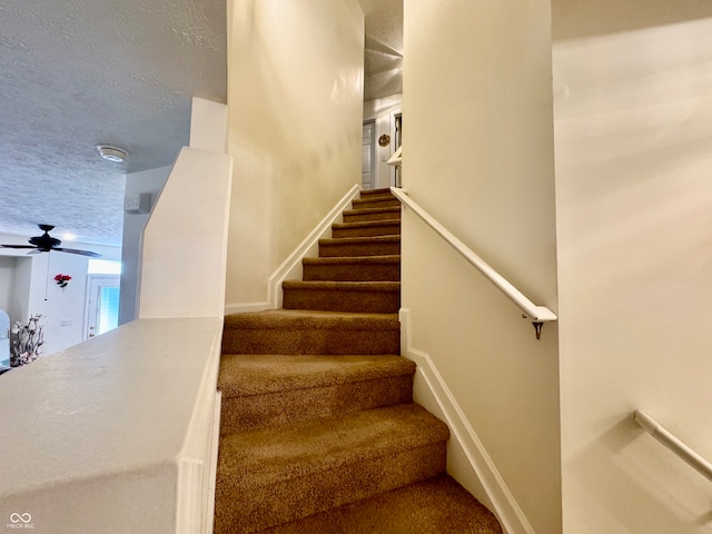 staircase with ceiling fan and a textured ceiling