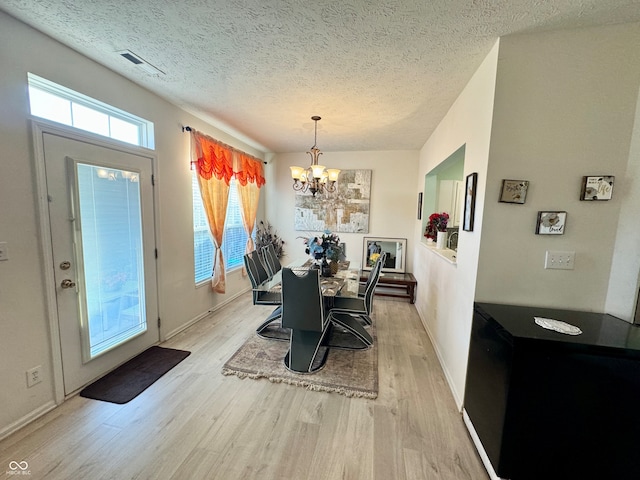 dining space with a notable chandelier, light hardwood / wood-style floors, and a textured ceiling