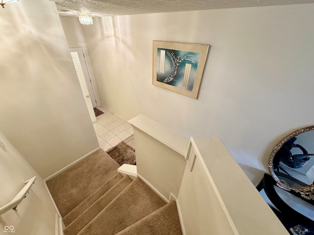 stairway with a textured ceiling and carpet flooring