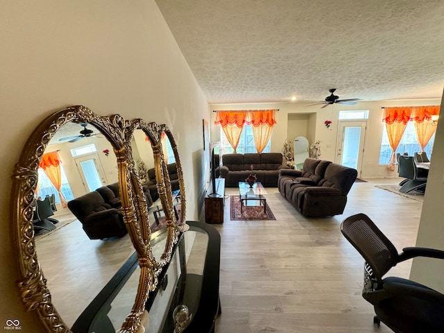 living room with ceiling fan, a textured ceiling, and light hardwood / wood-style flooring