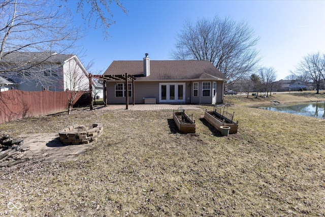 back of property with fence, an outdoor fire pit, a chimney, french doors, and a water view