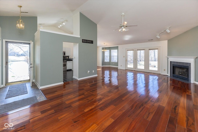 unfurnished living room featuring track lighting, wood finished floors, a tiled fireplace, and ceiling fan with notable chandelier