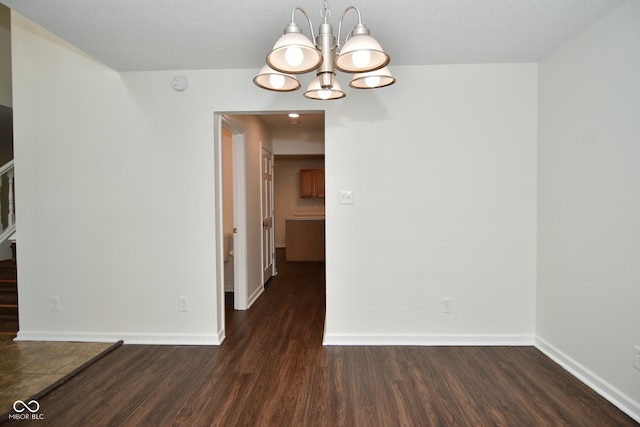 empty room featuring a notable chandelier, a textured ceiling, and dark hardwood / wood-style flooring