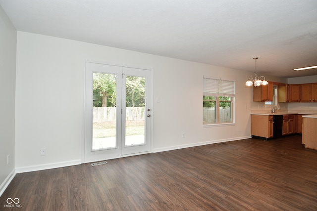 unfurnished living room featuring an inviting chandelier, a healthy amount of sunlight, dark wood-type flooring, and sink