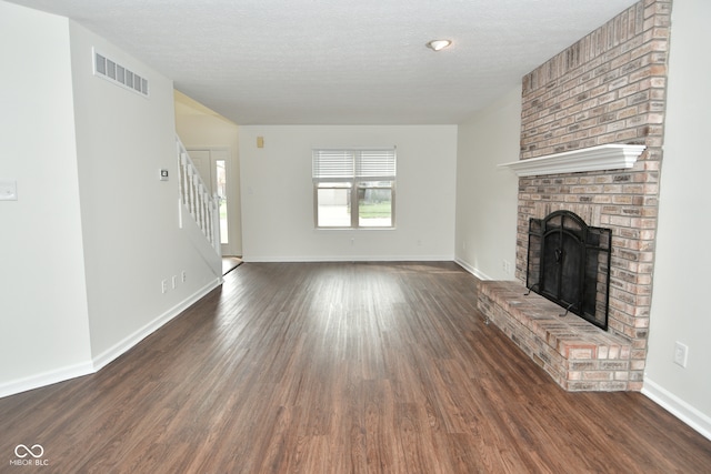 unfurnished living room featuring a brick fireplace, a textured ceiling, and dark hardwood / wood-style flooring