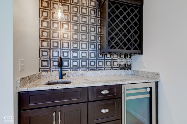 bar featuring light stone countertops, dark brown cabinetry, sink, pendant lighting, and wine cooler