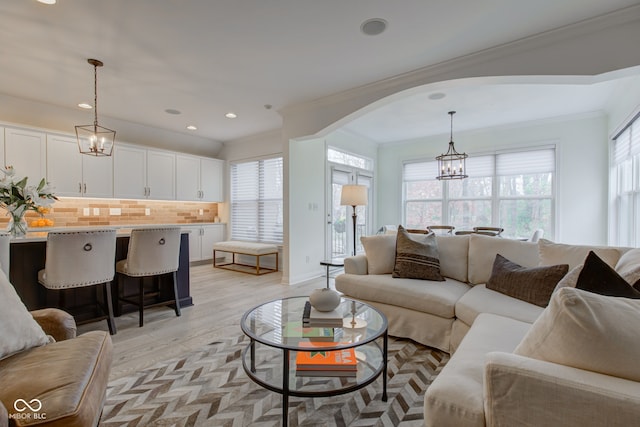 living room with light hardwood / wood-style flooring, ornamental molding, a chandelier, and a healthy amount of sunlight