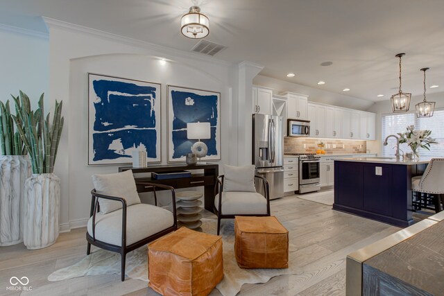 kitchen featuring stainless steel appliances, crown molding, pendant lighting, light hardwood / wood-style flooring, and white cabinetry