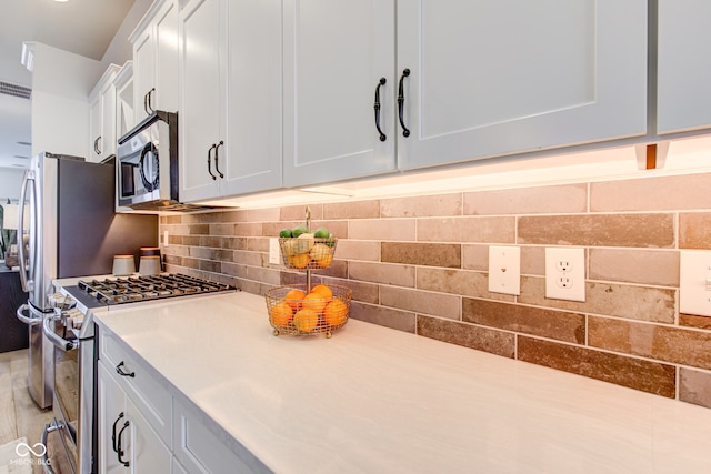 kitchen with tasteful backsplash, white cabinets, and appliances with stainless steel finishes