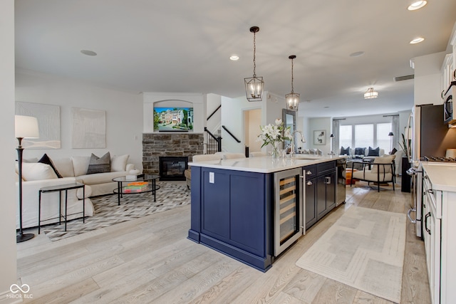 kitchen featuring a kitchen island with sink, beverage cooler, pendant lighting, white cabinets, and light hardwood / wood-style floors