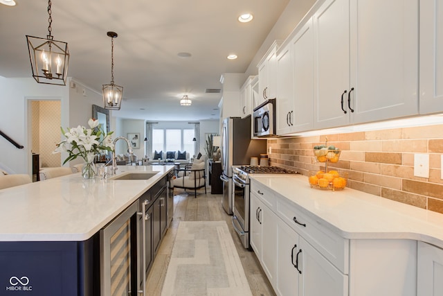 kitchen featuring light wood-type flooring, stainless steel appliances, sink, wine cooler, and hanging light fixtures