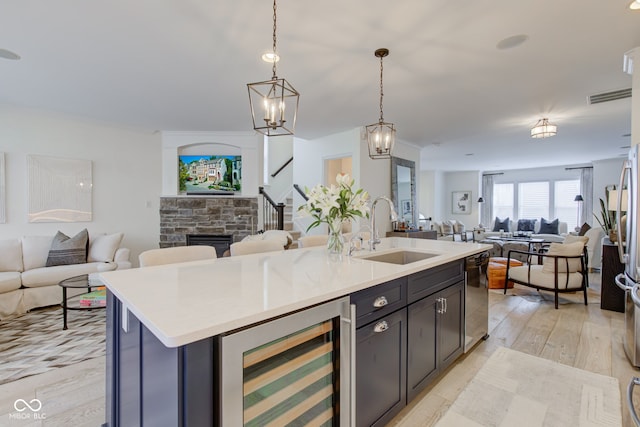 kitchen featuring beverage cooler, sink, hanging light fixtures, a kitchen island with sink, and light wood-type flooring