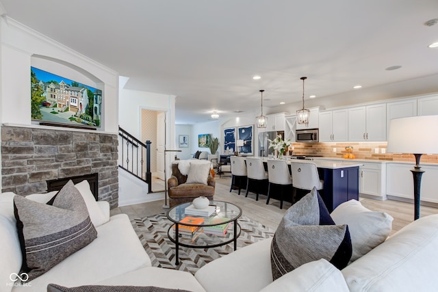 living room with a chandelier, light wood-type flooring, and a stone fireplace