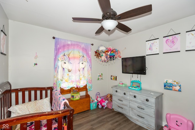 bedroom with a nursery area, ceiling fan, and wood finished floors