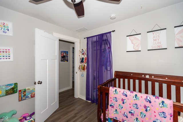 bedroom with a nursery area, ceiling fan, and dark wood-type flooring