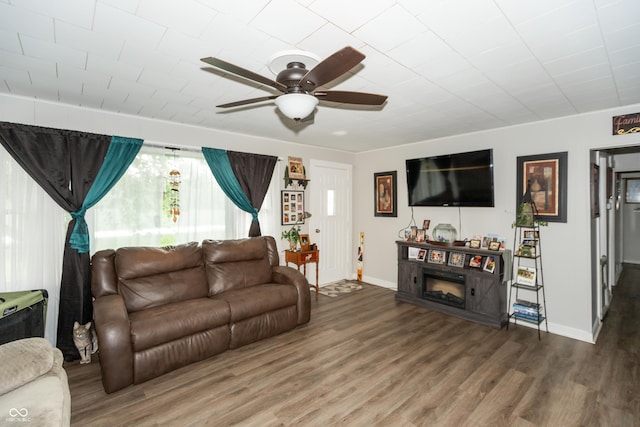 living area with a ceiling fan, a fireplace, baseboards, and wood finished floors