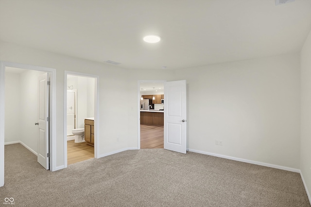 unfurnished bedroom featuring stainless steel fridge, ensuite bath, and light colored carpet