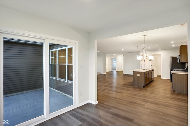 kitchen featuring hanging light fixtures, an inviting chandelier, a kitchen island with sink, dark wood-type flooring, and sink