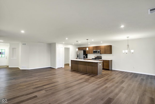 kitchen featuring appliances with stainless steel finishes, a center island with sink, hanging light fixtures, and dark wood-type flooring