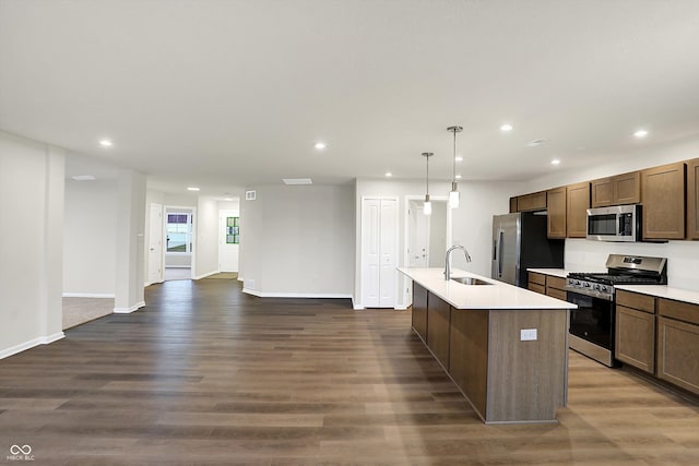 kitchen with a kitchen island with sink, hanging light fixtures, sink, appliances with stainless steel finishes, and dark hardwood / wood-style flooring