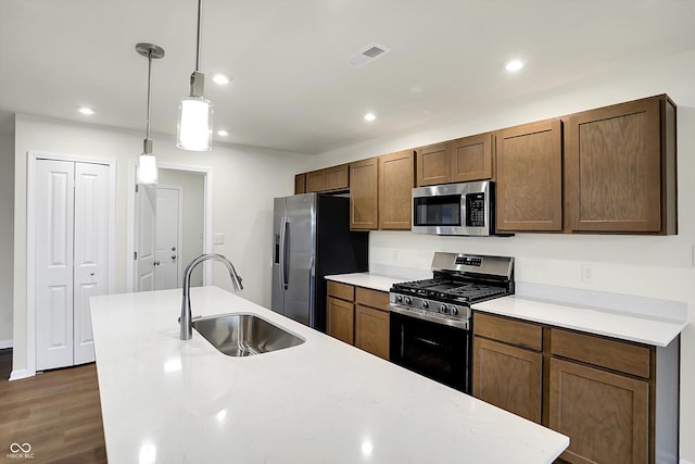 kitchen featuring sink, dark hardwood / wood-style flooring, stainless steel appliances, decorative light fixtures, and a center island with sink